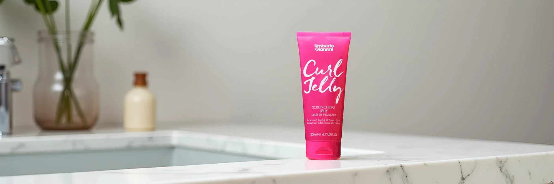 Umberto Giannini Curl Jelly hair product on a white marble bathroom counter