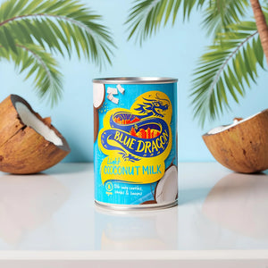 Blue Dragon light coconut milk can with coconuts and palm leaves on white table