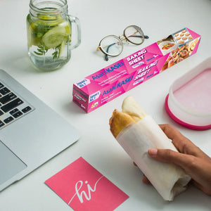 Hand holding a sandwich wrapped in baking sheet near laptop, jar of infused water, and glasses.