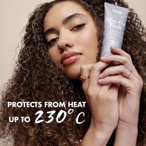 Woman with curly hair holding Umberto Giannini Blow Out Frizz heat protectant styling cream