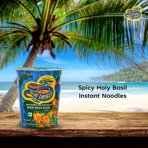 Blue Dragon Spicy Holy Basil instant noodles cup on a wooden table with tropical beach and palm tree background