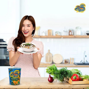 Smiling woman in kitchen holding bowl of Blue Dragon Spicy Holy Basil instant noodle soup
