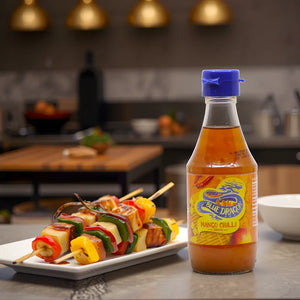 Bottle of Blue Dragon mango chilli sauce next to grilled vegetable skewers on a kitchen counter