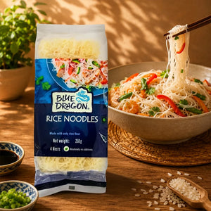 Blue Dragon Rice Noodles 250g pack with cooked noodles, shrimp, veggies, and chopsticks, served in a bowl with rice grains nearby.