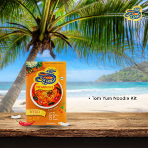 Blue Dragon Tom Yum Noodle Kit package on wooden table with tropical beach and palm tree background