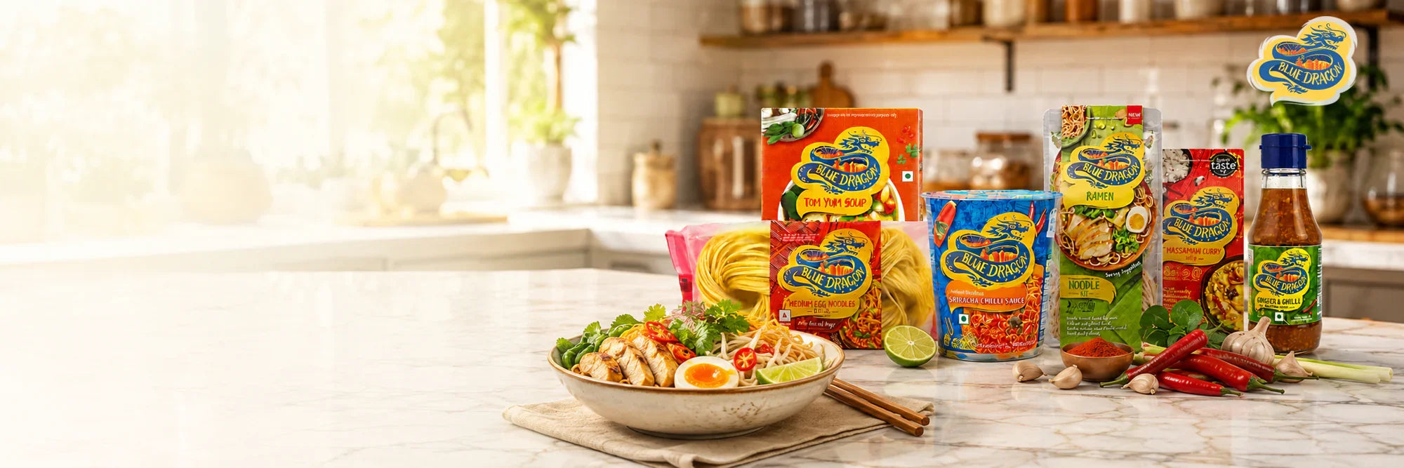 Blue Dragon Asian food products including ramen, curry, chili sauce, and noodles displayed with fresh ingredients on a kitchen counter