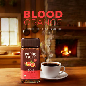 Coorg Valley Blood Orange instant coffee jar with steaming cup, cozy indoor fireplace setting