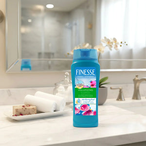 Finesse Volumizing Shampoo bottle on a bathroom counter with towels, soap, and orchid flowers