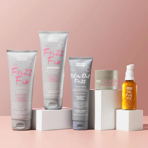 Umberto Giannini Frizz Fix hair care range with shampoo, conditioner, styling cream, control clay, and frizz oil on pink background