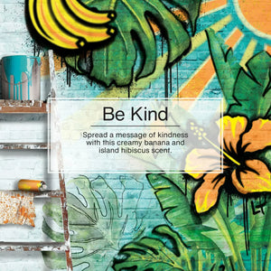 Colorful mural of bananas, hibiscus flower, and palm leaves with Be Kind message on brick wall.