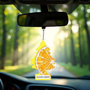 Car rearview mirror with hanging Little Trees air freshener featuring sliced lemon design in sunny forest road setting