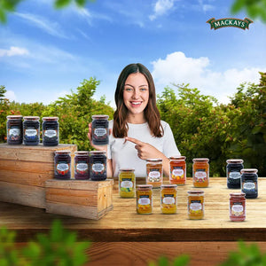 Woman holding and pointing at Mackays Cherries & Berries preserve jar with various Mackays jam jars displayed outdoors