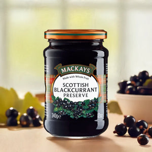 Jar of Mackays Scottish Blackcurrant Preserve with blackcurrants around on wooden surface