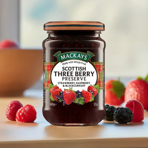 Jar of Mackays Scottish Three Berry Preserve with strawberries, raspberries, and blackcurrants on wooden table