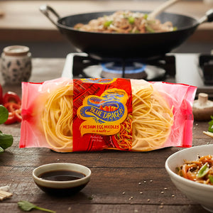Blue Dragon Medium Egg Noodles pack on wooden table with sauce, stir fry in wok and bowl
