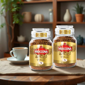 Two jars of Moccona Classic Medium Roast instant coffee on a wooden table with a white coffee cup and saucer in a cozy kitchen setting