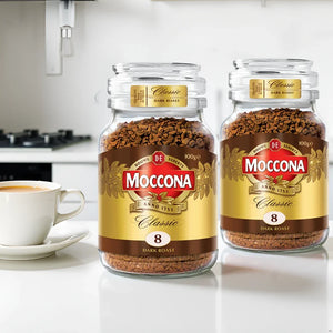 Two jars of Moccona Classic Dark Roast instant coffee 100g on kitchen counter with white cup of coffee