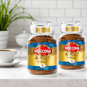 Two jars of Moccona Classic Decaffeinated instant coffee placed on a kitchen counter with a white coffee cup and green plant in background