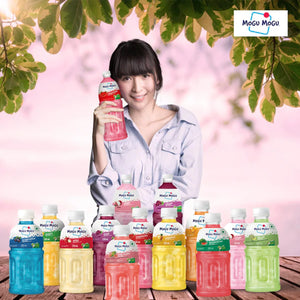 Woman holding Mogu Mogu pink guava drink with various colorful Mogu Mogu fruit flavors on wooden table