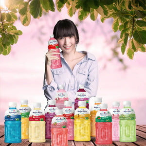 Smiling woman holding pink Mogu Mogu drink with various colorful fruit-flavored Mogu Mogu bottles on wooden table