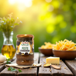 Jar of Sacla Black Summer Truffle pesto on wooden table with pasta, cheese, oil, and herbs in background