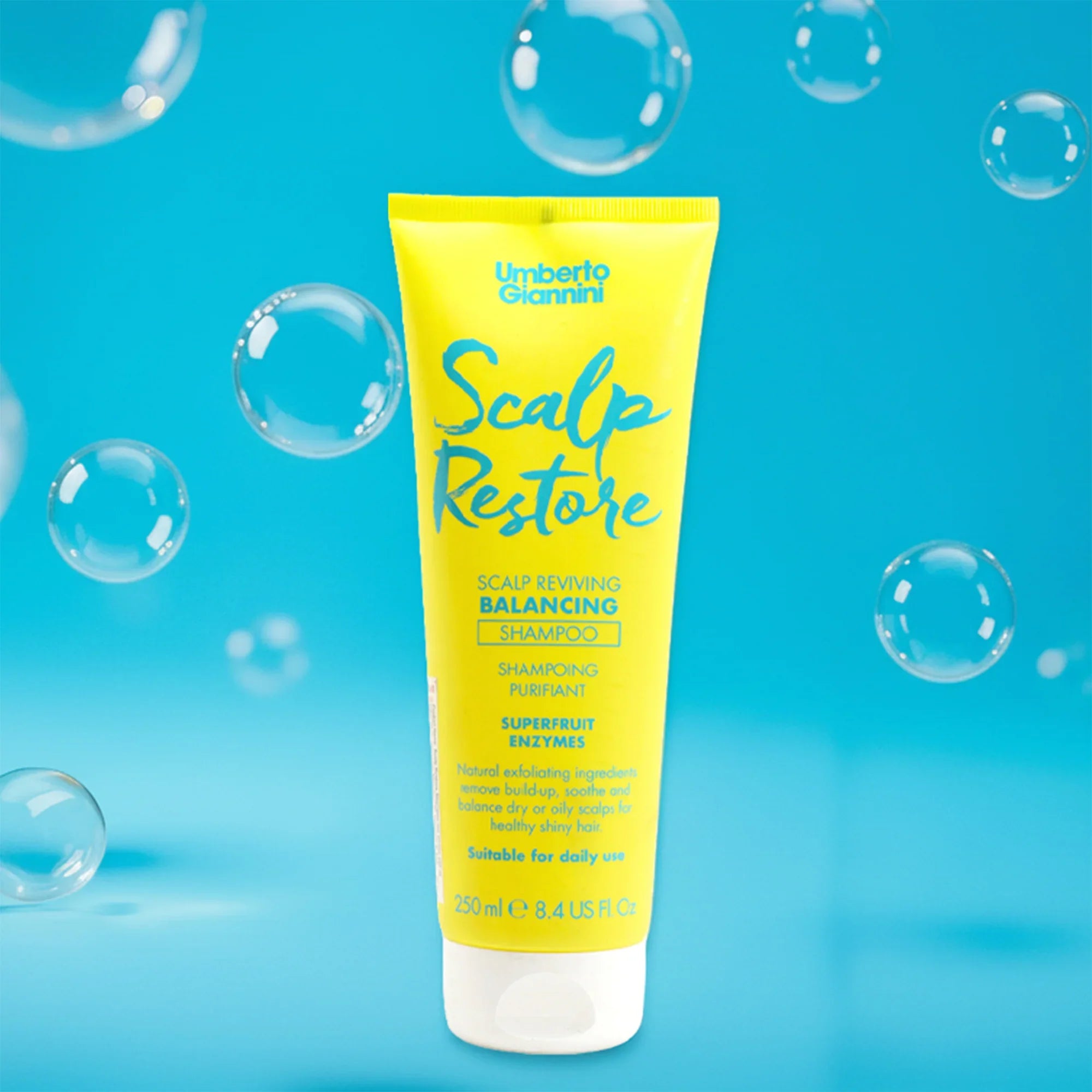 Yellow tube of Umberto Giannini Scalp Restore Balancing Shampoo with bubbles on blue background