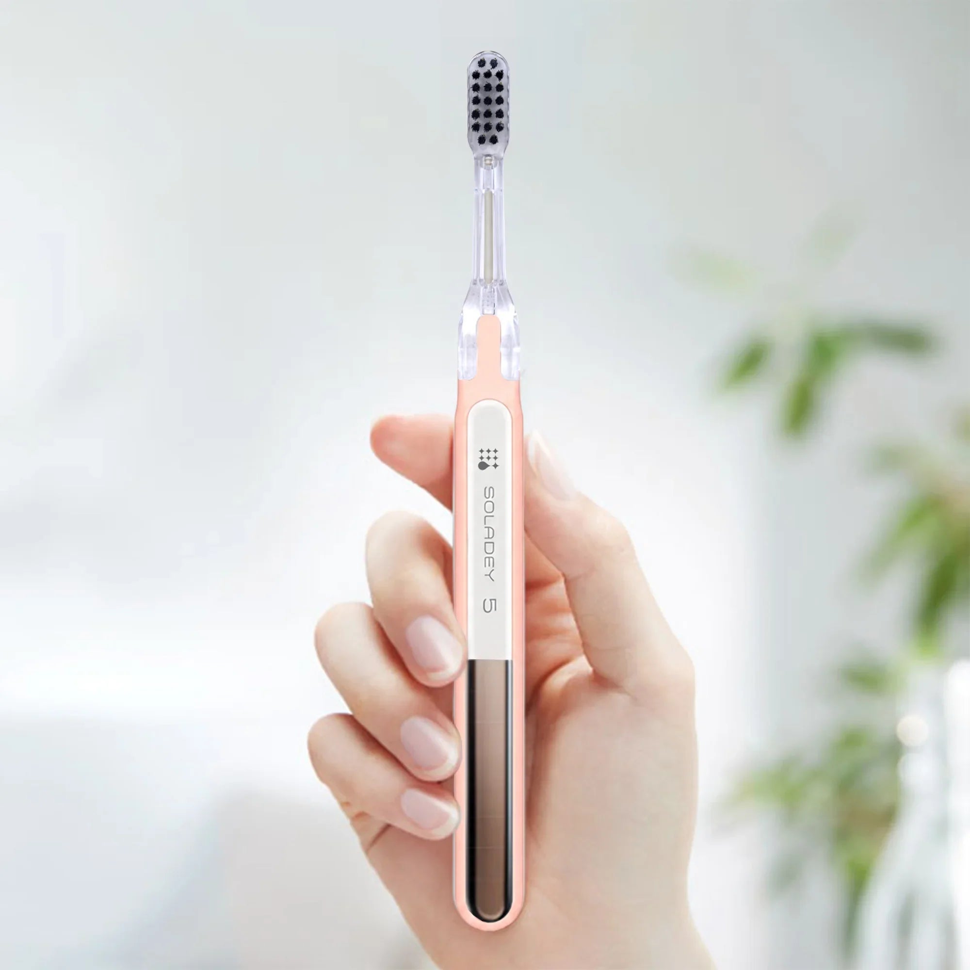 Hand holding a pink Soladey 5 sonic toothbrush against a soft blurred background.