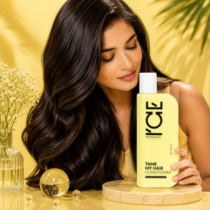 Woman with shiny wavy hair posing next to a bottle of ICE Professional Tame My Hair Conditioner.