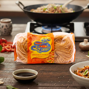 Pack of Blue Dragon wholewheat noodles on wooden table with pan cooking noodles and soy sauce bowl