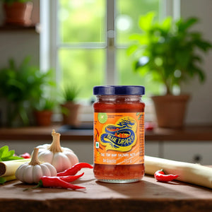 Jar of Blue Dragon Thai Tom Yum culinary paste surrounded by garlic, red chili peppers, and lemongrass on kitchen counter