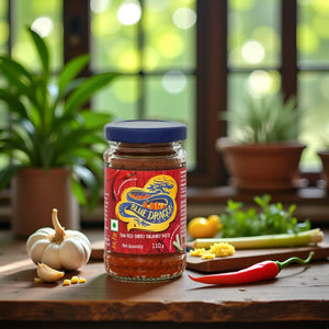 Blue Dragon Thai red curry paste jar on wooden table with garlic, chili pepper and fresh herbs