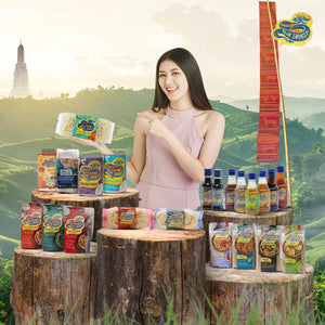 Smiling woman presenting Blue Dragon Asian food products including noodles, sauces, and coconut milk on wooden stumps