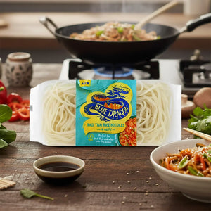 Pack of Blue Dragon Pad Thai rice noodles on wooden table with cooked noodles and skillet in background
