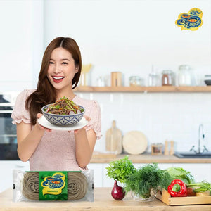 Smiling woman holding bowl of soba noodle salad in modern kitchen with Blue Dragon noodles and fresh vegetables