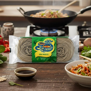 Blue Dragon package of soba noodles on wooden table with cooked noodles in bowl and wok on stove