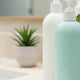 Hair conditioner bottles with pump dispensers on a bathroom counter beside a sink and plant