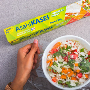 Hand using food wrap on fresh salad bowl, Asahi KASEI premium wrap box visible