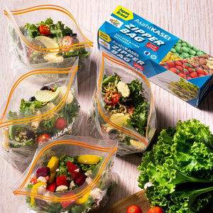 Four clear zipper bags filled with fresh salad beside Asahi Kasei Zipper Bag box on a table