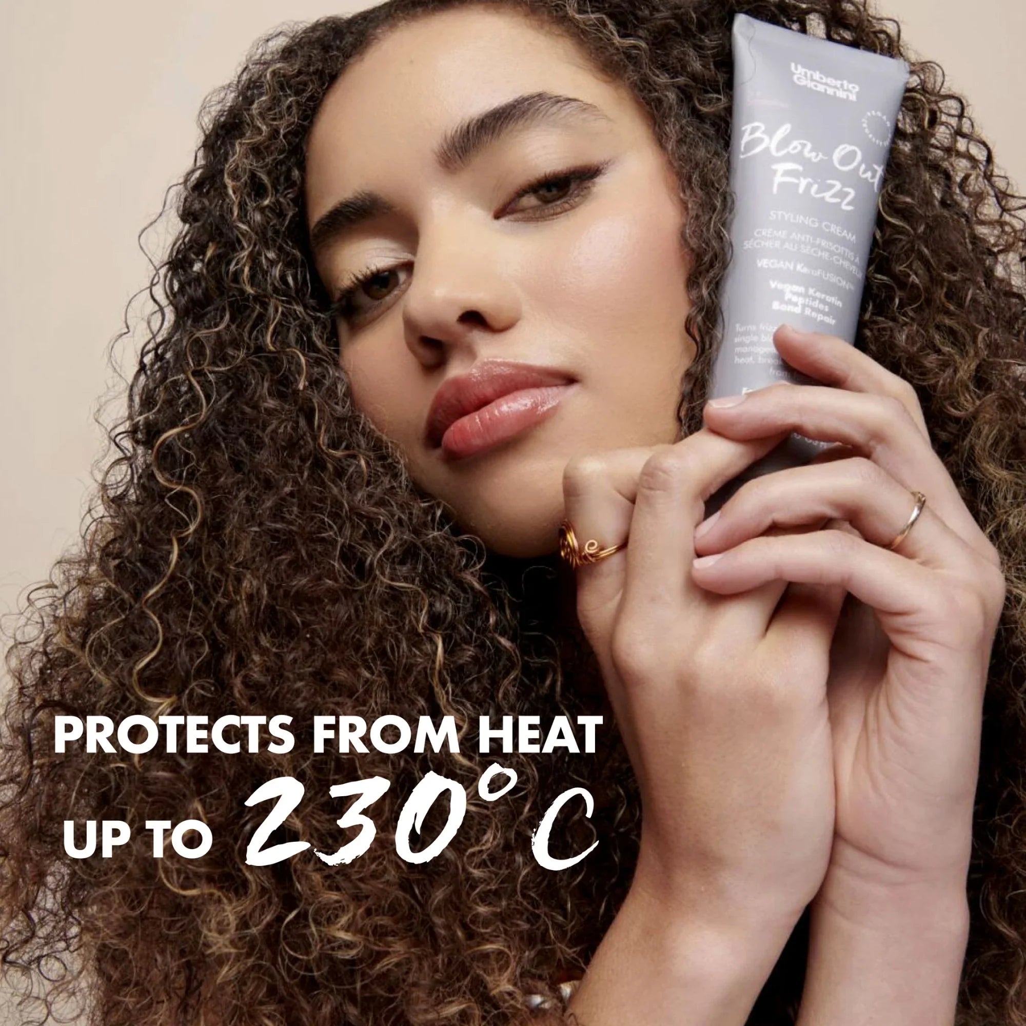 Woman with curly hair holding Umberto Giannini Blow Out Frizz heat protectant styling cream