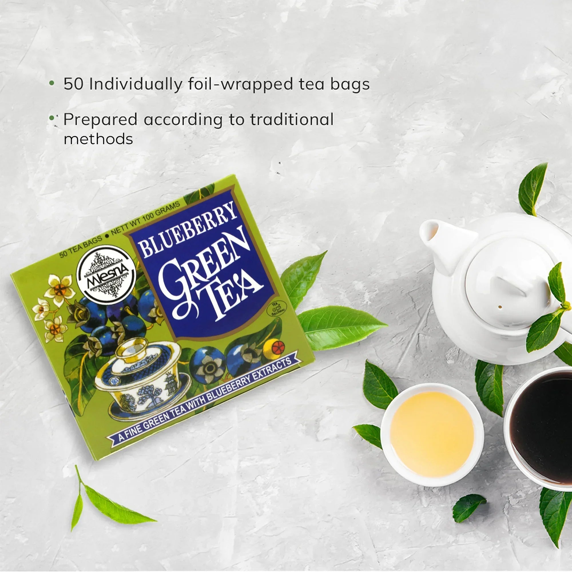Box of blueberry green tea with teapot, tea cups, and green leaves on a light background