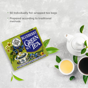 Box of blueberry green tea with teapot, tea cups, and green leaves on a light background