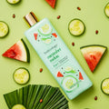 Bodycology Cucumber Melon 2-in-1 body wash and bubble bath bottle on a green background with cucumber slices and watermelon pieces.