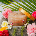 Body scrub jar with flowers and green leaves on a stone surface