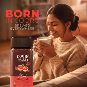 Woman enjoying a cup of Coorg Valley Blood Orange instant coffee, cozy indoor setting.