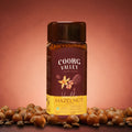 Coorg Valley Vanilla Hazelnut instant coffee jar with hazelnuts on a brown background