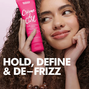 Woman with curly hair holding Umberto Giannini Crème de Curl Control Cream against pink background with 'Hold, Define & De-Frizz' text