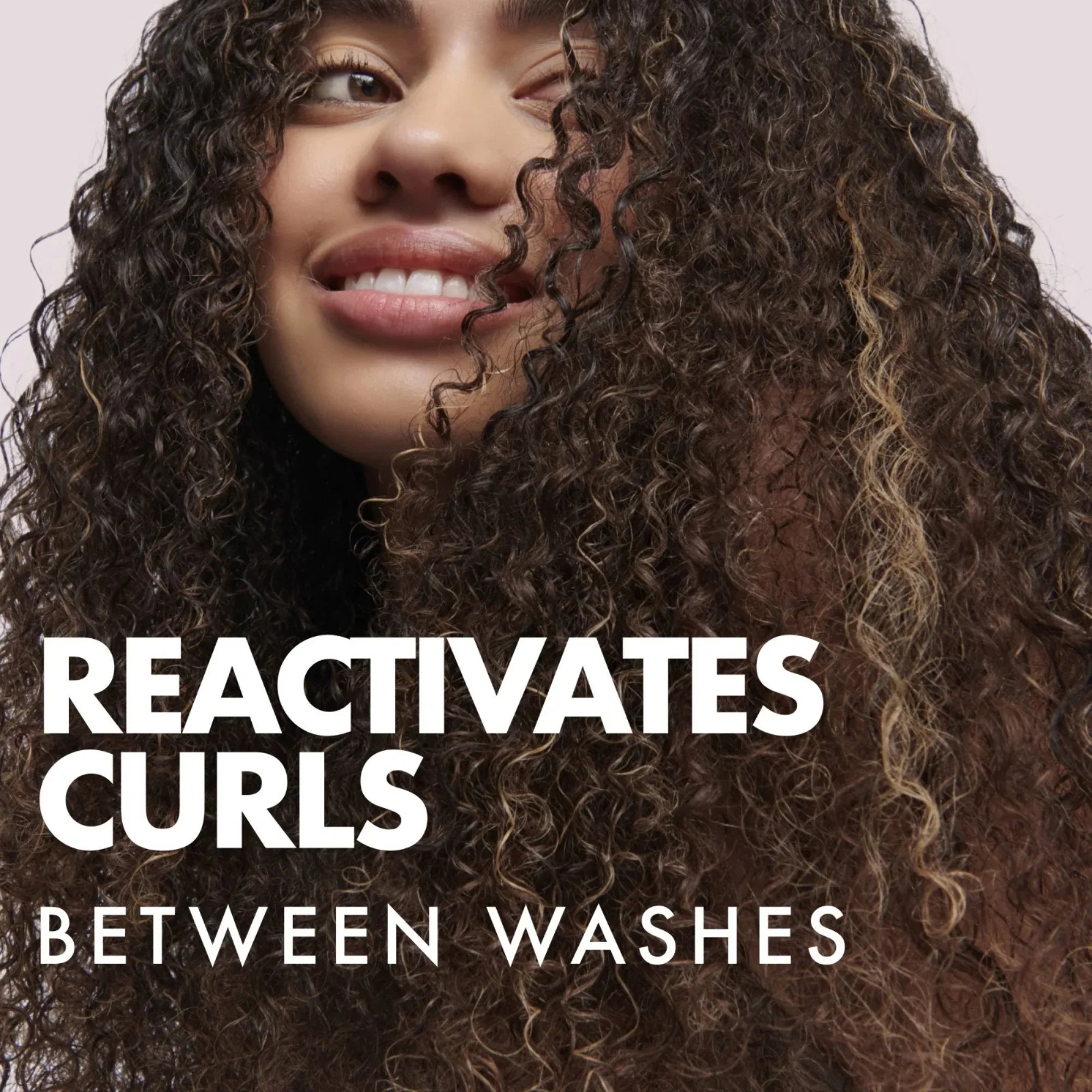 Smiling woman with thick, defined curly hair highlighting curl reactivating spray for hair care