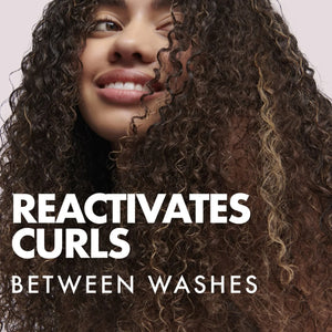 Smiling woman with thick, defined curly hair highlighting curl reactivating spray for hair care