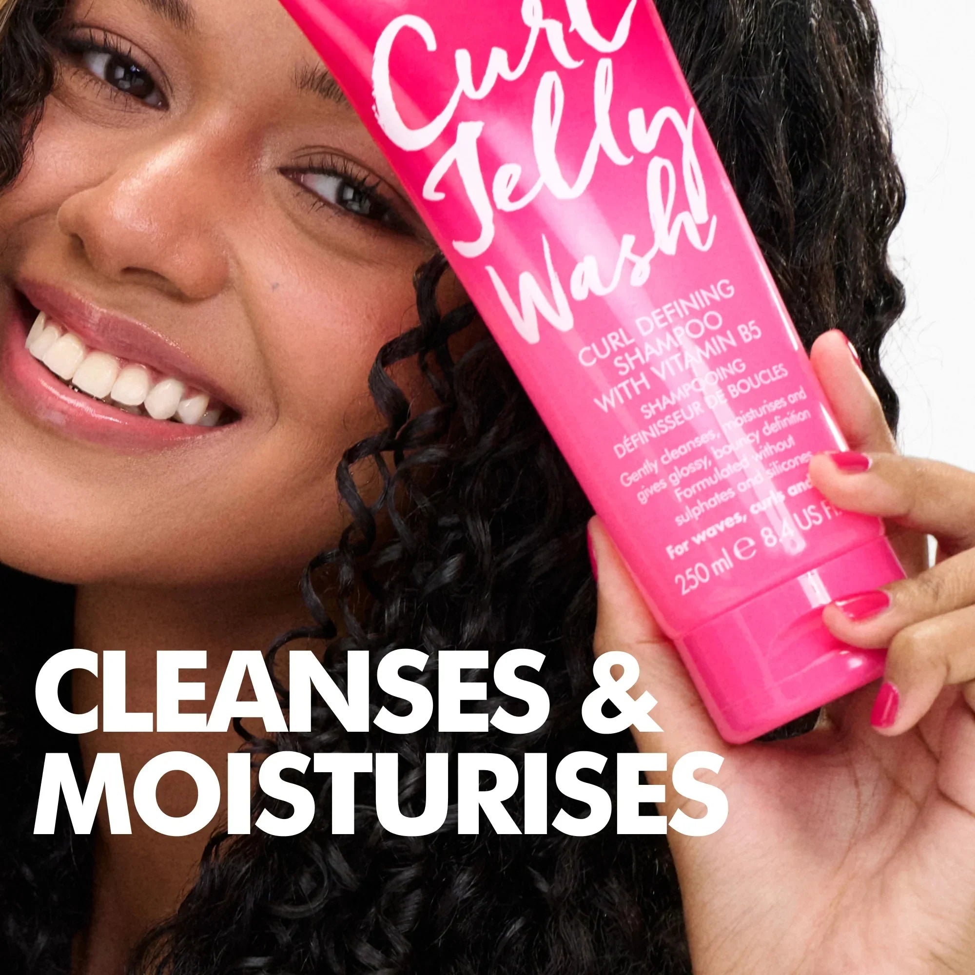 Smiling woman with curly hair holding pink Curl Jelly Wash shampoo with vitamin B5, text 'Cleanses & Moisturises'