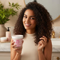 Smiling woman with curly hair holding Umberto Giannini Curl Magic Hydro Curly Treatment Mask in a stylish bathroom